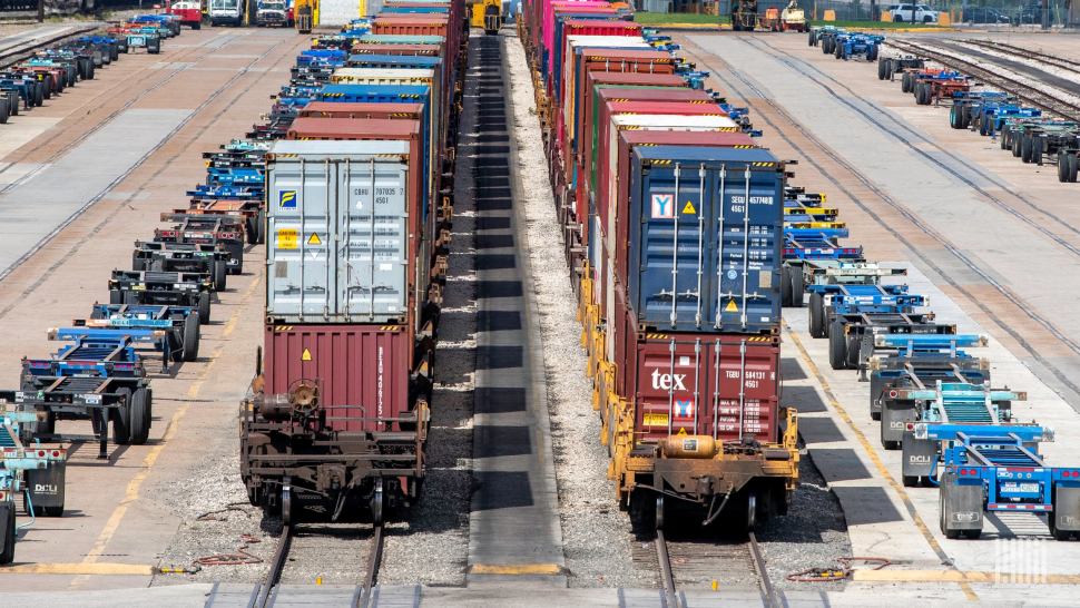 Double-stack container trains beside rows of container chassis in an intermodal yard